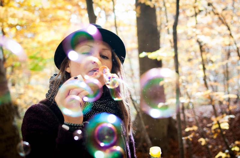 Raphaela holding a bubble wand in an autumn forest, surrounded by floating bubbles and golden leaves, evoking playfulness, reflection, and the beauty of change