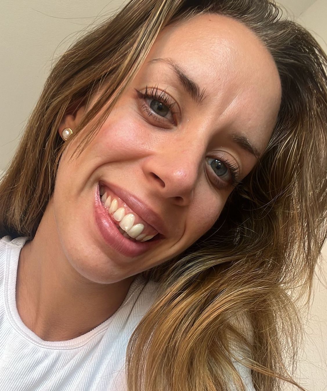 Bianca from Australia smiling warmly in a close-up portrait, with long light brown hair, pearl earrings, and a white top against a softly lit background.