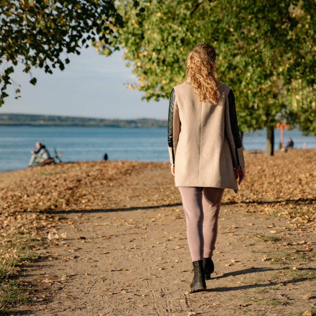 Person walking along a leaf-covered path beside a lake on an autumn day