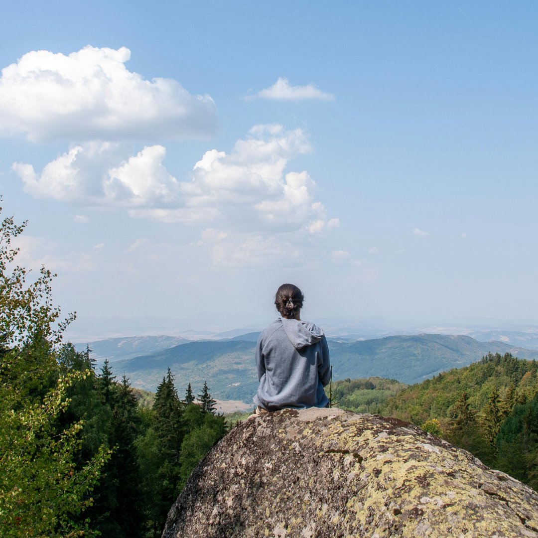 Person sitting on a rock overlooking a wide landscape of hills and sky