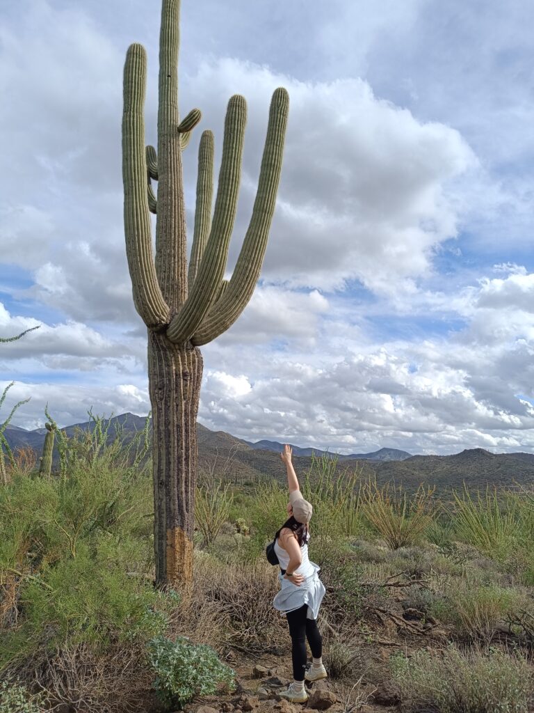 Raphaela standing beside a tall saguaro cactus in the Sonoran Desert landscape